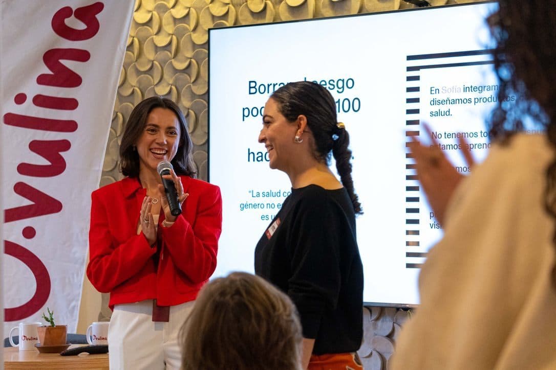 Valeria y Noelia al frente de una plática, junto al banner de Ovulina