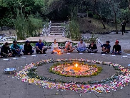 Círculo alrededor de un mandala de flores y una vela, al caer la tarde