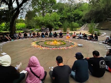 Grupo numeroso sentado en círculo alrededor de un mandala de flores